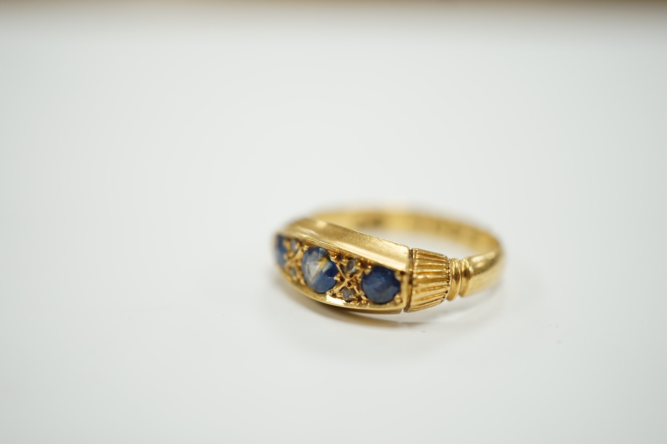 A George V 18ct gold and three stone sapphire set ring, with diamond chip spacers, size K, gross weight 3.3 grams.